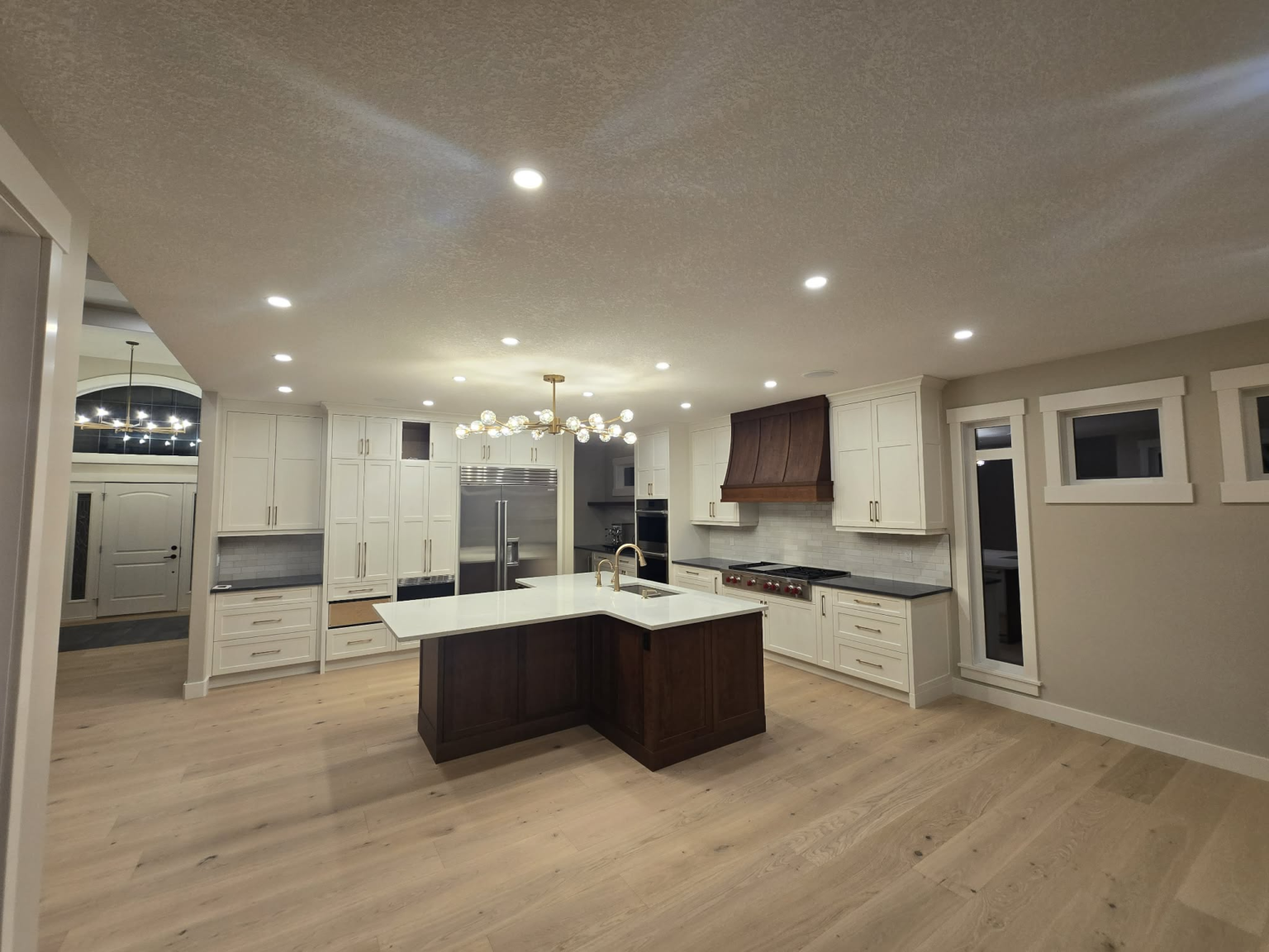 Bright kitchen cabinetry with white perimeter cabinets, a dark wood island and brass fixtures