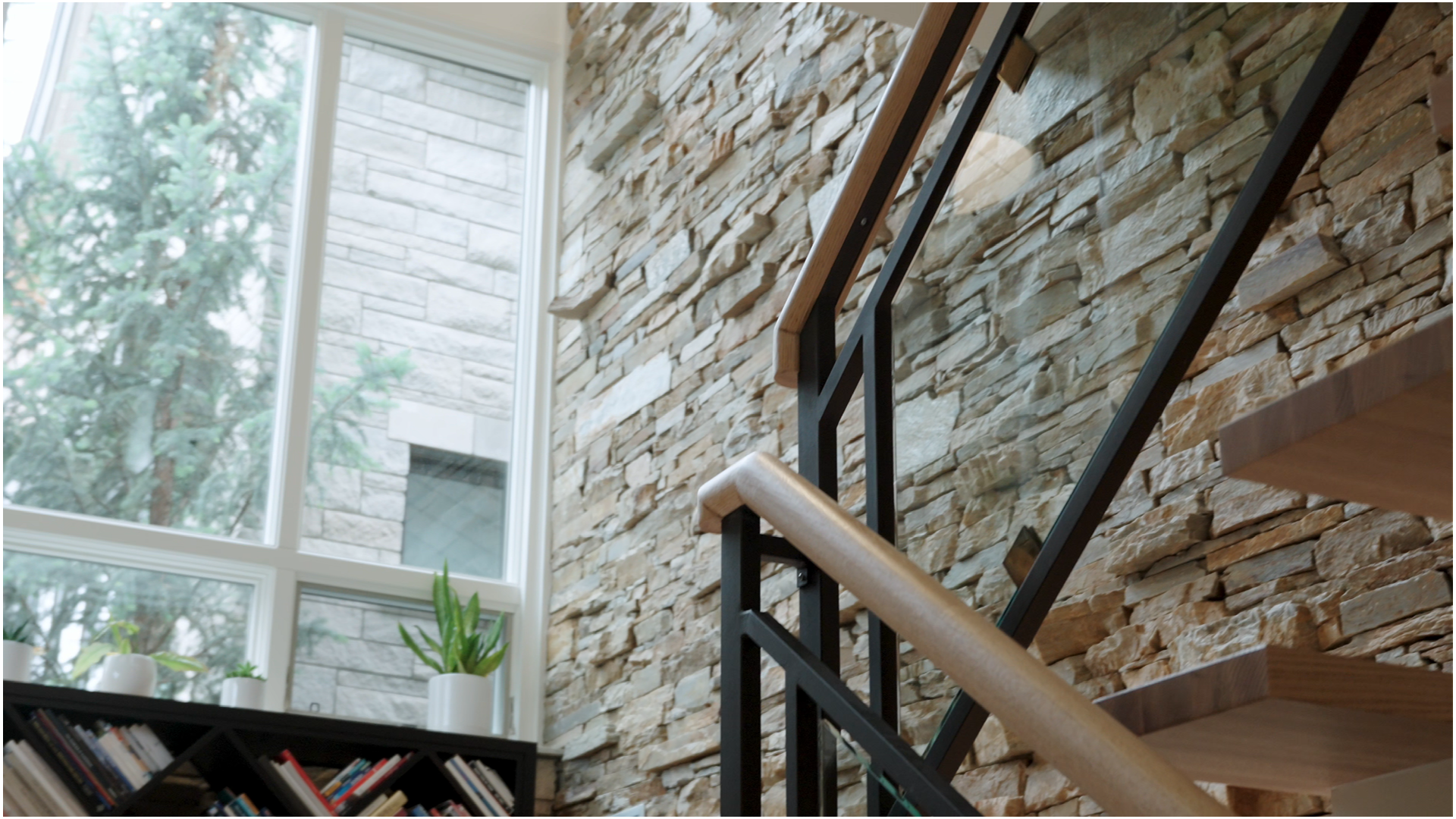 Modern Calgary staircase with natural stone feature wall, black railing, and light wood handrail.