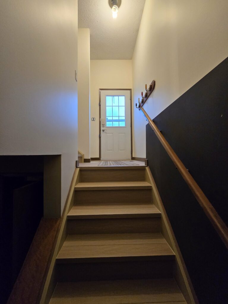 Updated stair flight with light flooring, painted walls, dark lower wall and wood handrail