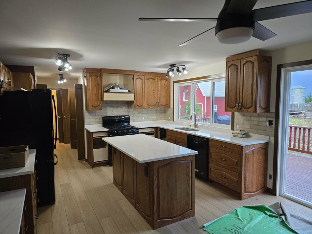 Central late-stage kitchen view emphasizing the island, white countertops, backsplash and light flooring