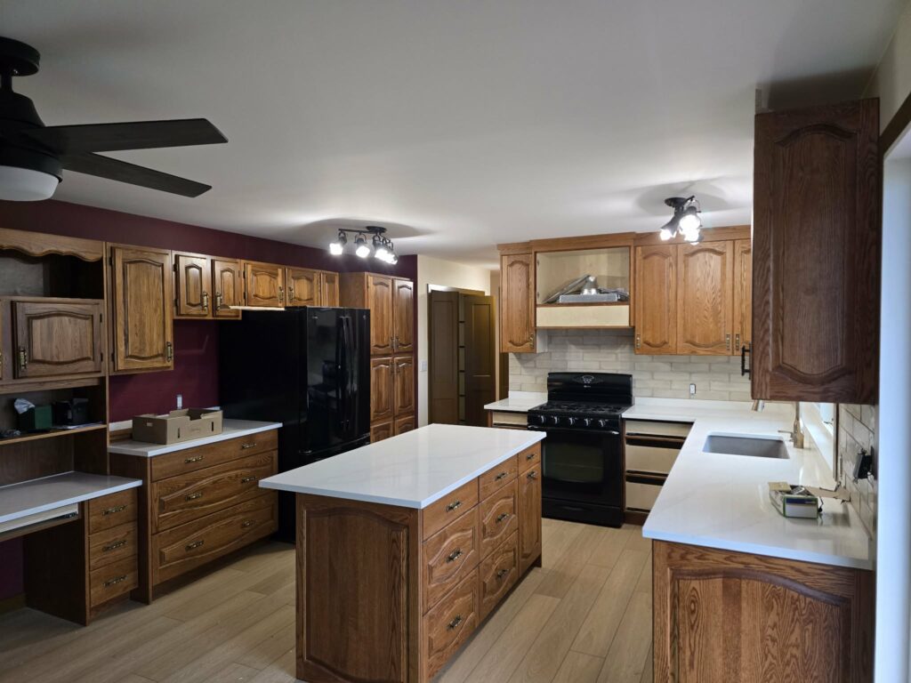 Reverse late-stage kitchen view showing the island, counters, lighting and retained wood character