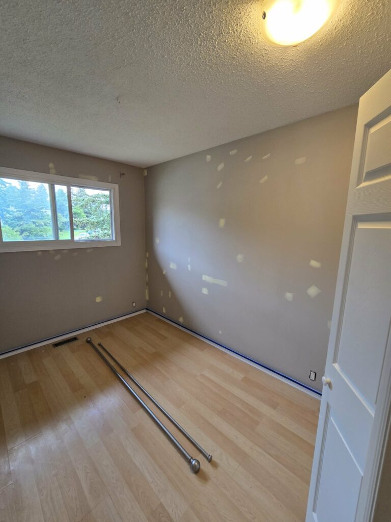 Bedroom wall preparation beside a replacement window with masking at the baseboard